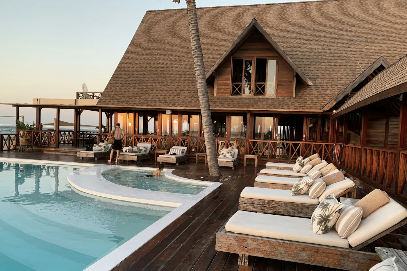 Lounge chairs along a hotel pool, with a wooden building behind them
